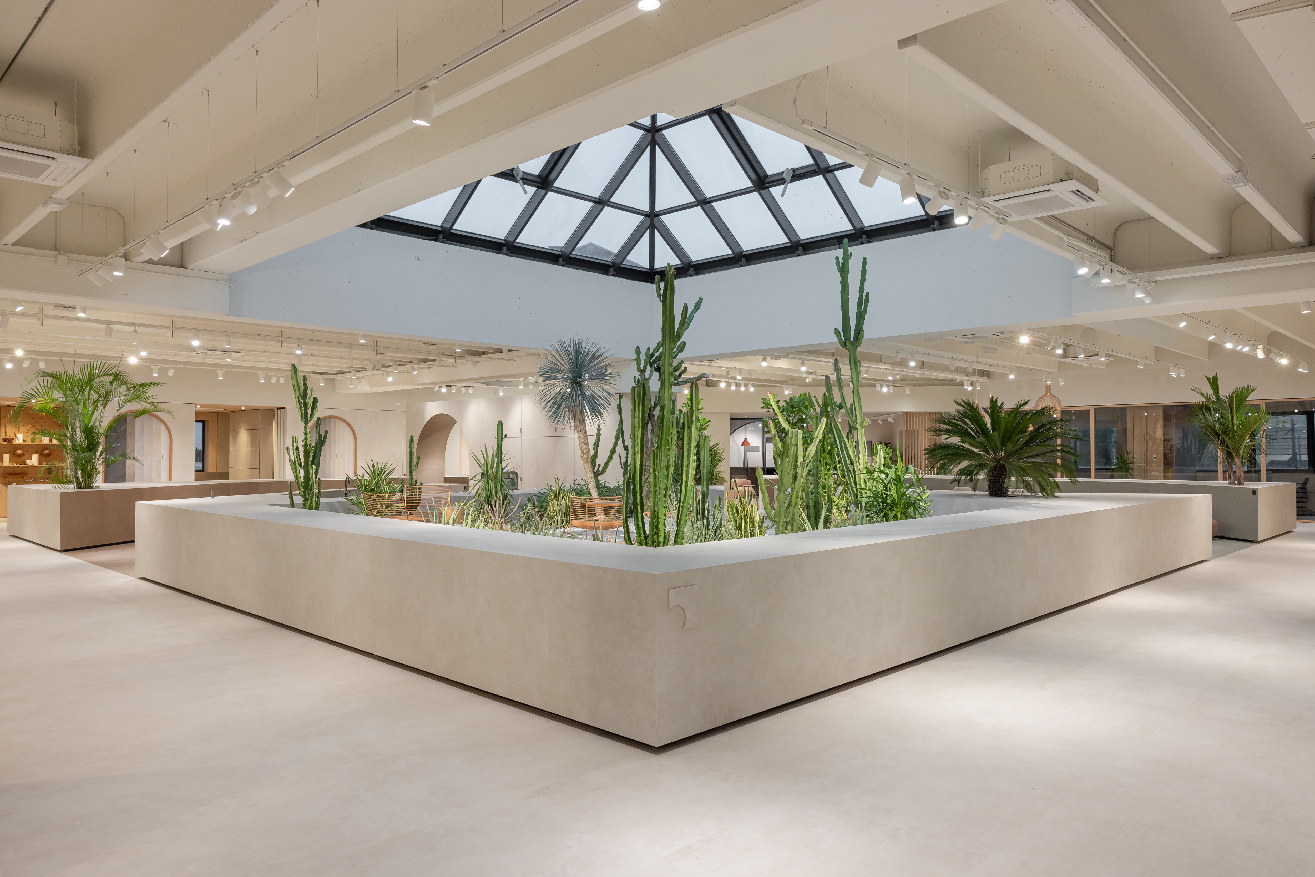 Bright, modern showroom with large-format tiles, plant island, and skylight for an open sense of space.