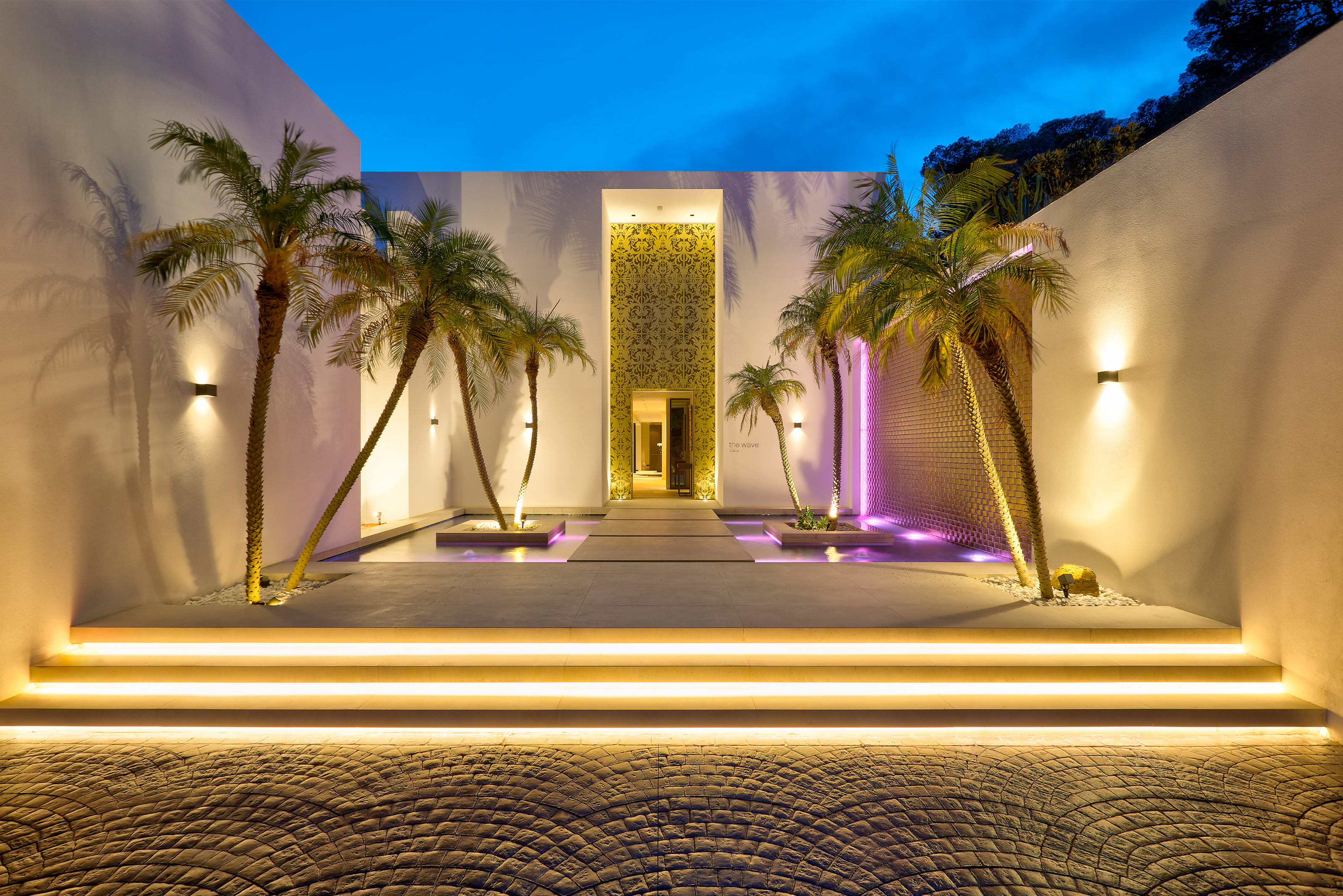 Exclusive outdoor entrance with modern tiles, palms, and atmospheric lighting.