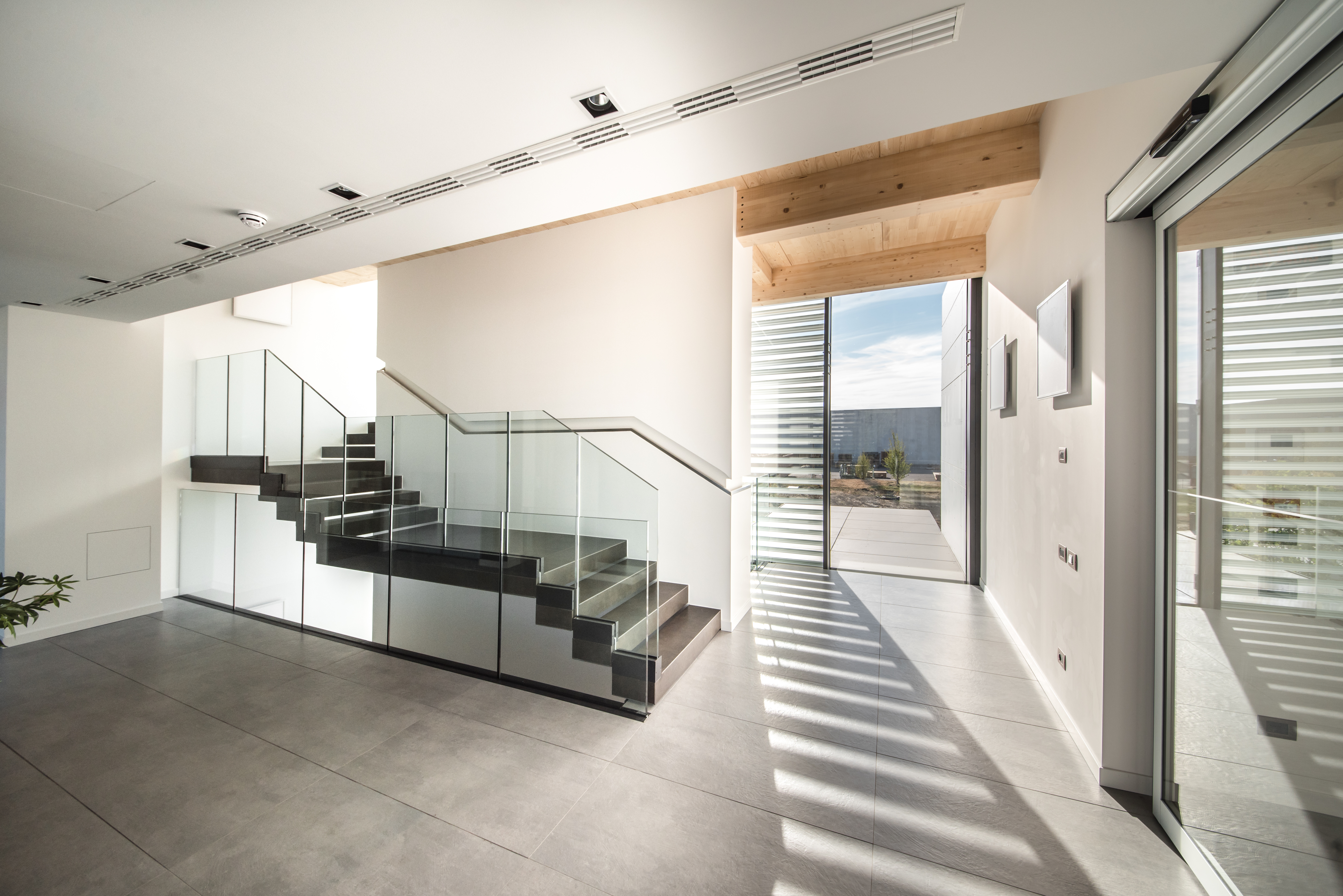 High-quality concrete-look floor tiles in a modern foyer with an elegant glass staircase.