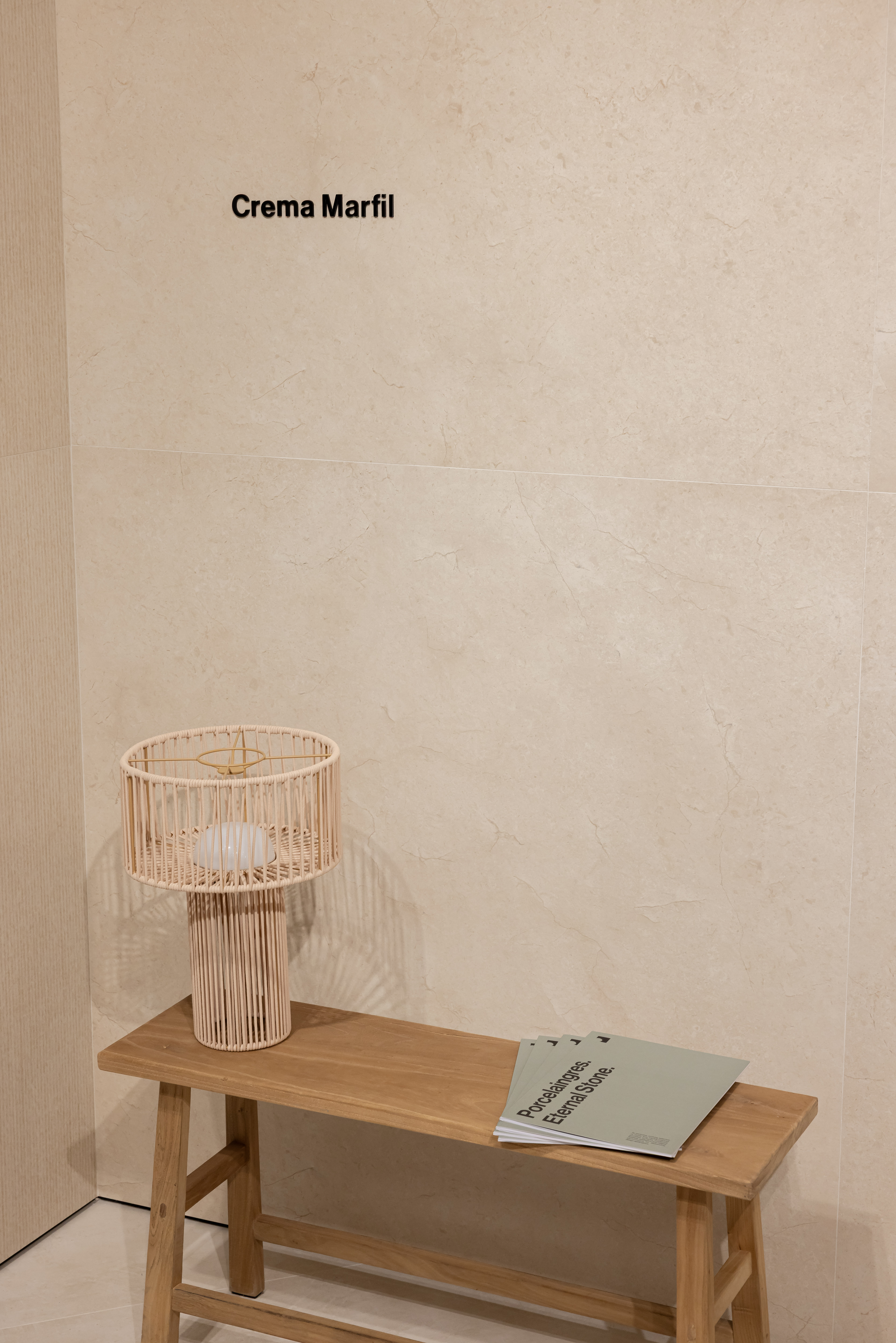 Bright Porcelaingres 'Crema Marfil' wall tiles, with wooden bench and lamp.
