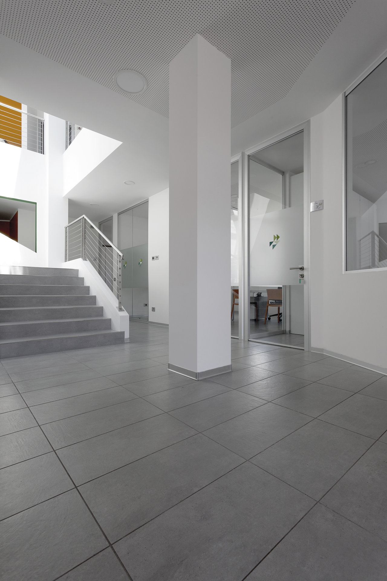 Large-format grey floor tiles in a bright, modern foyer with stairs.